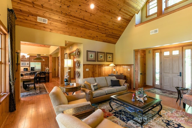 living area with high vaulted ceiling, a wainscoted wall, light wood-type flooring, wooden ceiling, and wood walls