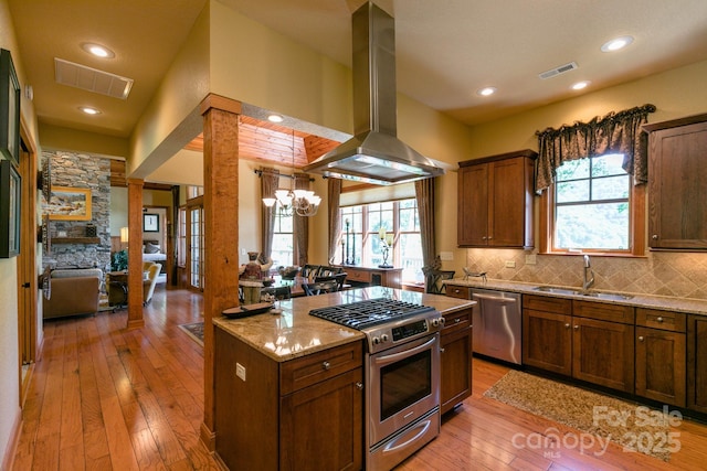 kitchen with appliances with stainless steel finishes, a sink, island exhaust hood, light wood-type flooring, and light stone countertops
