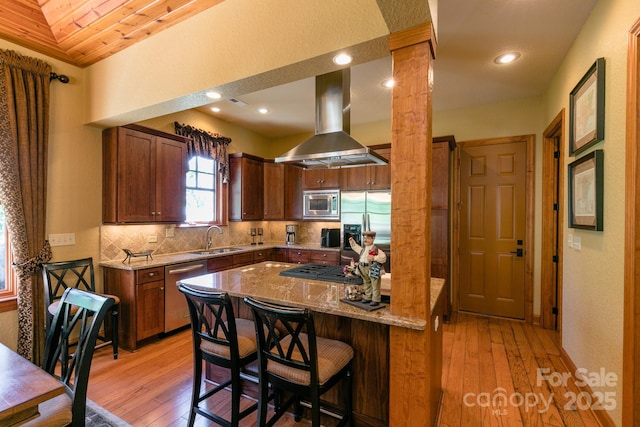 kitchen featuring appliances with stainless steel finishes, island range hood, ornate columns, a sink, and light stone countertops