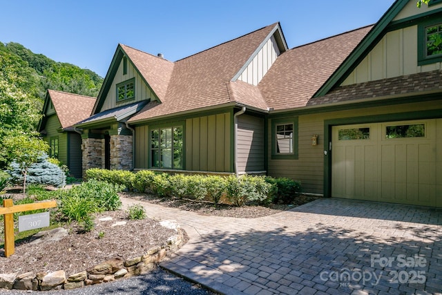 view of front of home featuring board and batten siding, roof with shingles, decorative driveway, and an attached garage