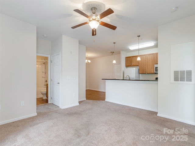 unfurnished living room featuring light carpet, ceiling fan, a chandelier, and baseboards