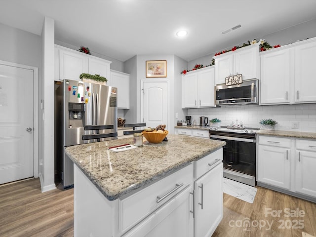 10426 Kempsford Dr, Charlotte, NC 28262 - kitchen featuring appliances with stainless steel finishes, a kitchen island, white cabinets, light wood-type flooring, and backsplash