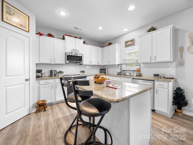 10426 Kempsford Dr, Charlotte, NC 28262 - kitchen featuring appliances with stainless steel finishes, a kitchen bar, a center island, white cabinets, and decorative backsplash