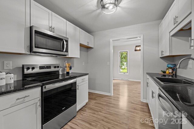 13446 Idlefield Ln, Matthews, NC 28105 - kitchen with stainless steel appliances, a sink, white cabinets, light wood-style floors, and dark stone countertops