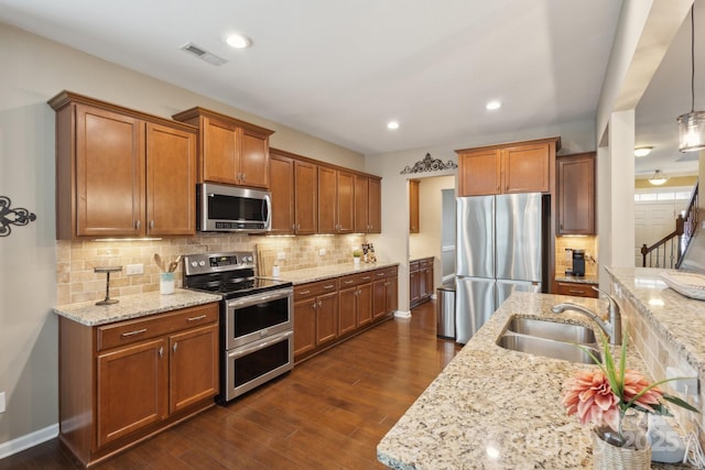4430 Bravery Pl SW, Concord, NC 28027 - kitchen with appliances with stainless steel finishes, a sink, brown cabinets, tasteful backsplash, and light stone counters