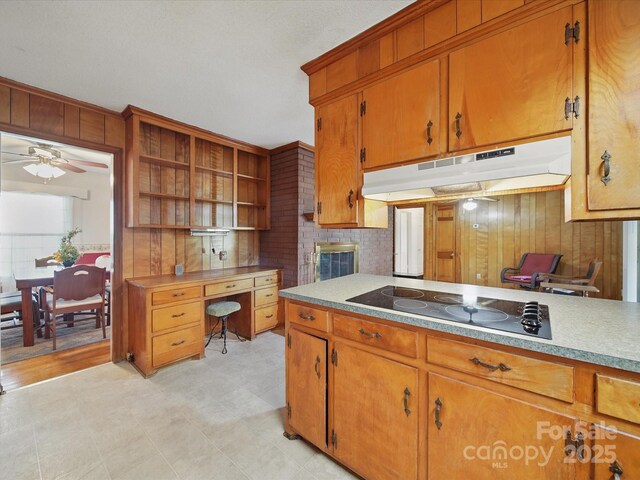 2216 Griffith Rd, Monroe, NC 28112 - kitchen featuring under cabinet range hood, black electric stovetop, brown cabinetry, light countertops, and wooden walls