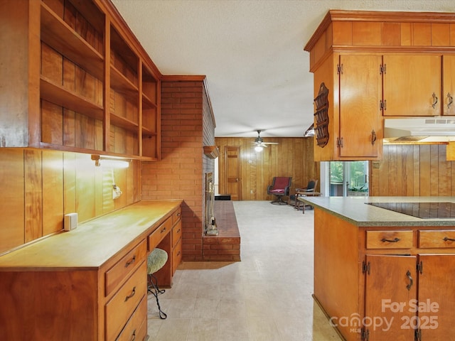 2216 Griffith Rd, Monroe, NC 28112 - kitchen featuring under cabinet range hood, black electric cooktop, brown cabinets, a ceiling fan, and wooden walls