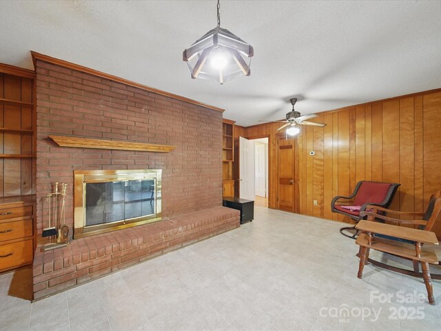 2216 Griffith Rd, Monroe, NC 28112 - unfurnished living room featuring a brick fireplace, wood walls, a ceiling fan, and a textured ceiling