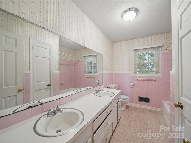 2216 Griffith Rd, Monroe, NC 28112 - full bath with wallpapered walls, tile walls, double vanity, shower / tub combination, and wainscoting