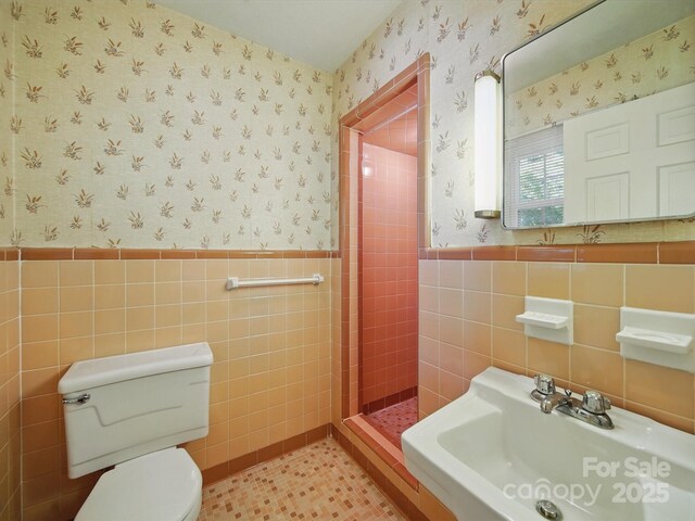 2216 Griffith Rd, Monroe, NC 28112 - bathroom with wallpapered walls, tile walls, toilet, wainscoting, and a sink