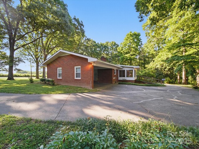 2216 Griffith Rd, Monroe, NC 28112 - view of property exterior with brick siding, asphalt driveway, a chimney, an attached carport, and a yard