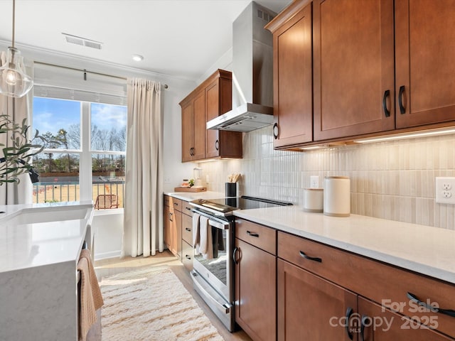 5508 Swaling St, Charlotte, NC 28217 - kitchen with stainless steel range with electric stovetop, wall chimney exhaust hood, backsplash, brown cabinetry, and pendant lighting