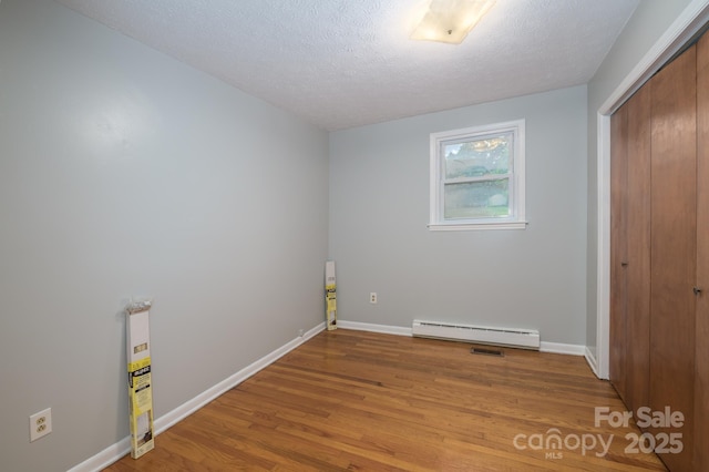 unfurnished bedroom featuring a baseboard heating unit, light wood-type flooring, a closet, baseboards, and a textured ceiling