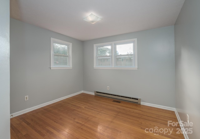 spare room featuring a baseboard heating unit, baseboards, and light wood-style floors
