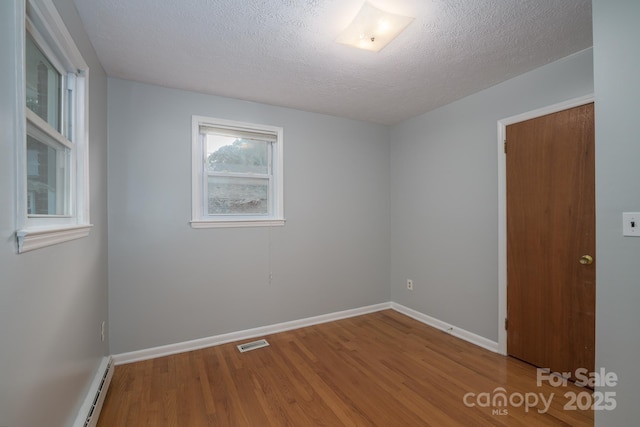 unfurnished room with wood finished floors, baseboard heating, a textured ceiling, and baseboards