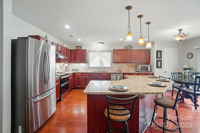 512 Nanny Point Dr, Monroe, NC 28110 - kitchen with stainless steel appliances, under cabinet range hood, backsplash, wood finished floors, and hanging light fixtures