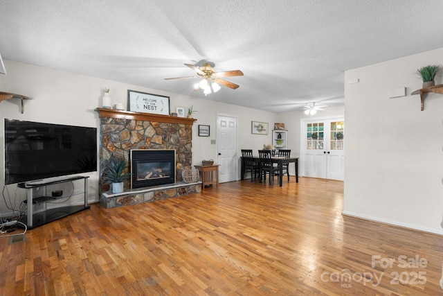 139 Pleasant Garden Dr, Taylorsville, NC 28681 - living room featuring ceiling fan, wood finished floors, a stone fireplace, a textured ceiling, and baseboards