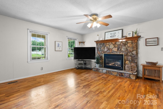 139 Pleasant Garden Dr, Taylorsville, NC 28681 - living area with wood finished floors, a ceiling fan, a stone fireplace, baseboards, and a textured ceiling