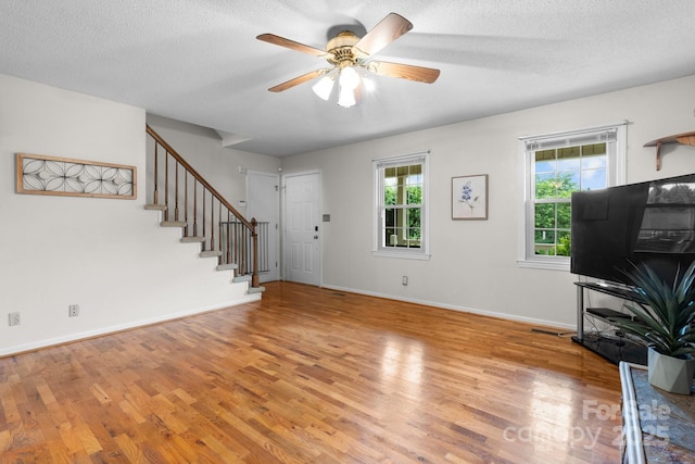 139 Pleasant Garden Dr, Taylorsville, NC 28681 - unfurnished living room with light wood-type flooring, stairway, a ceiling fan, baseboards, and a textured ceiling