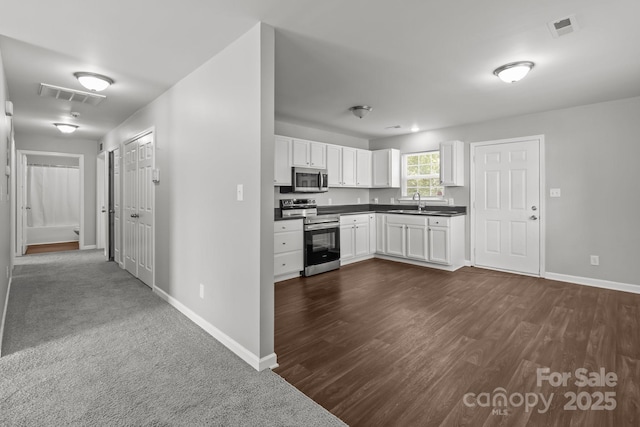 252 Sweet Bay Ln NW, Concord, NC 28027 - kitchen with stainless steel appliances, baseboards, dark countertops, white cabinetry, and dark wood-style flooring