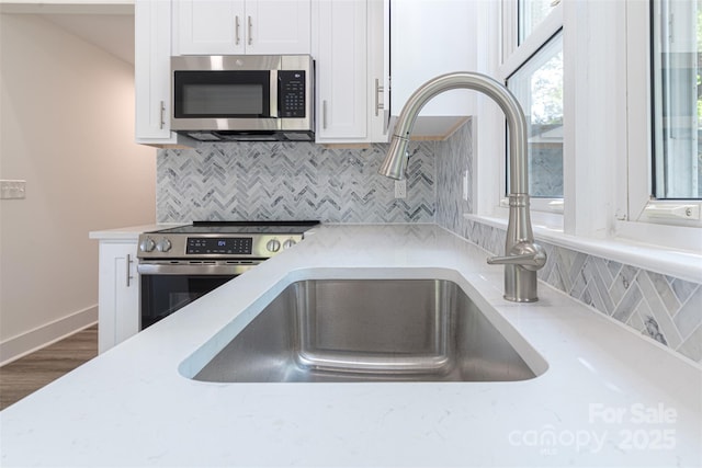615 Irish Potato Rd, Concord, NC 28025 - kitchen with stainless steel appliances, a sink, white cabinets, tasteful backsplash, and wood finished floors