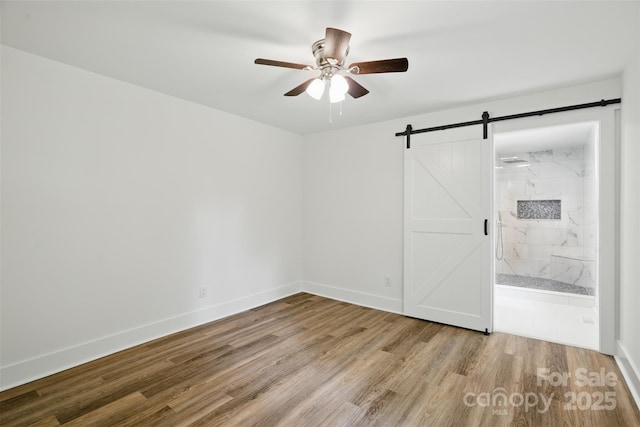 615 Irish Potato Rd, Concord, NC 28025 - unfurnished bedroom featuring wood finished floors, a barn door, baseboards, connected bathroom, and a ceiling fan