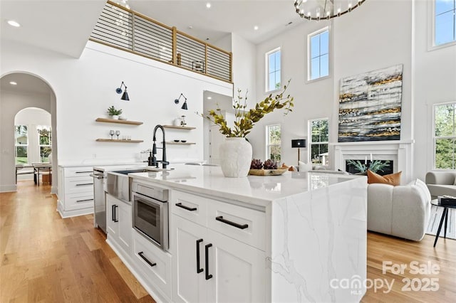 621 Poindexter Dr, Charlotte, NC 28209 - kitchen with arched walkways, light wood finished floors, white cabinets, a high ceiling, and light stone counters