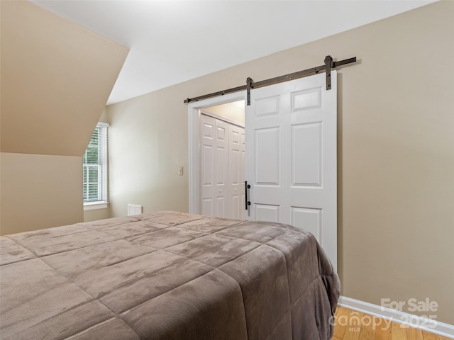 1493 Upper Browns Creek Rd, Burnsville, NC 28714 - bedroom featuring a barn door, wood finished floors, baseboards, vaulted ceiling, and a closet