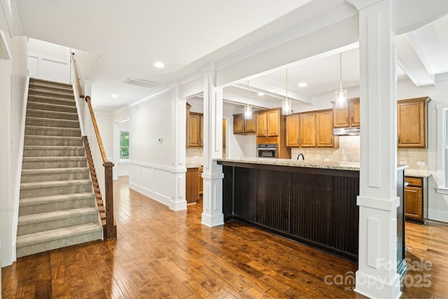 8521 Aspen Ct, Charlotte, NC 28227 - kitchen with stainless steel oven, brown cabinets, dark wood finished floors, under cabinet range hood, and crown molding