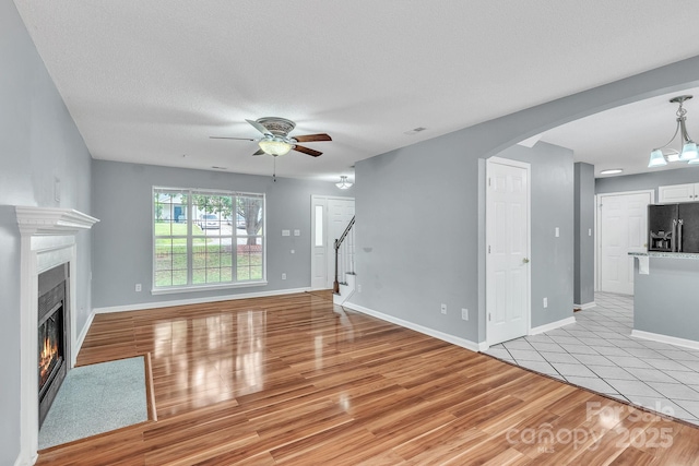 8120 Vermilion Dr, Charlotte, NC 28215 - unfurnished living room featuring ceiling fan, light wood-style flooring, arched walkways, a lit fireplace, and stairway