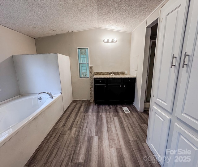 1145 Daniel Rd, Mocksville, NC 27028 - bathroom with lofted ceiling, wood finished floors, a bath, vanity, and a textured ceiling