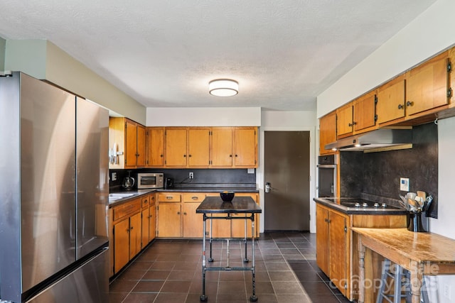 318 Old Leicester Hwy, Asheville, NC 28806 - kitchen with appliances with stainless steel finishes, under cabinet range hood, brown cabinets, dark countertops, and dark tile patterned floors