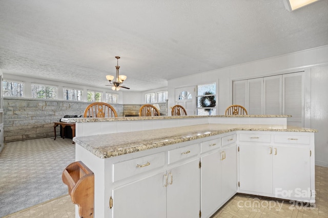 2866 Old Morganton Rd, Lenoir, NC 28645 - kitchen featuring a chandelier, a textured ceiling, open floor plan, light stone counters, and white cabinetry