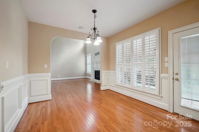 100 Woodwinds Dr, Mount Holly, NC 28120 - unfurnished dining area with light wood finished floors, wainscoting, arched walkways, a decorative wall, and a glass covered fireplace