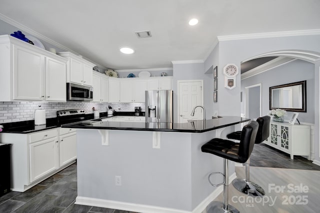 2224 Hartwell Ln, Fort Mill, SC 29707 - kitchen featuring appliances with stainless steel finishes, arched walkways, a kitchen bar, white cabinetry, and dark countertops