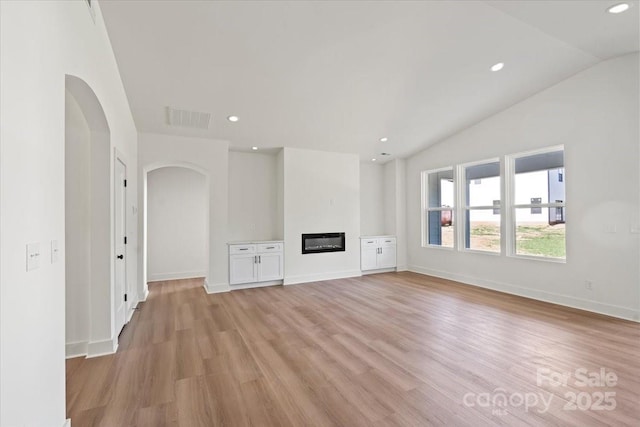 8632 Cedarbrook Dr, Charlotte, NC 28215 - unfurnished living room featuring arched walkways, light wood-type flooring, lofted ceiling, a glass covered fireplace, and recessed lighting