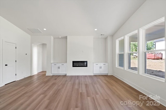 8632 Cedarbrook Dr, Charlotte, NC 28215 - unfurnished living room with light wood-style floors, arched walkways, a glass covered fireplace, baseboards, and recessed lighting