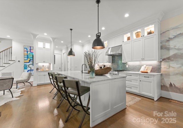 1160 S Kings Dr, Charlotte, NC 28207 - kitchen with ventilation hood, backsplash, a center island with sink, white cabinetry, and light wood-style floors