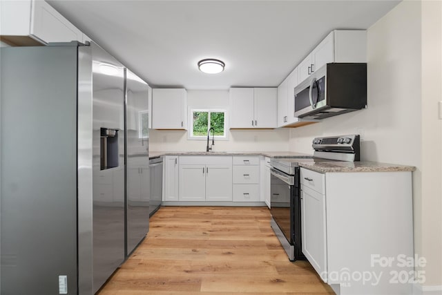 94 Camp Branch Rd, Black Mountain, NC 28711 - kitchen with appliances with stainless steel finishes, white cabinetry, light wood finished floors, and light stone counters