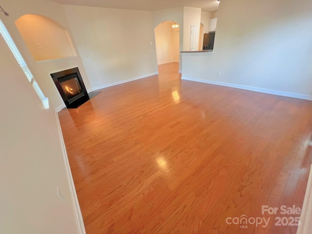 11624 Truan Ln, Cornelius, NC 28031 - unfurnished living room with arched walkways, light wood-style flooring, baseboards, and a fireplace with flush hearth