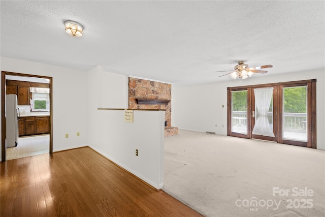 2309 Potter Rd S, Waxhaw, NC 28173 - unfurnished living room featuring plenty of natural light, a ceiling fan, a textured ceiling, a stone fireplace, and baseboards