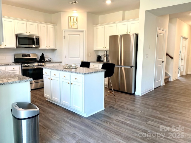 7024 Wheyfield Dr, Charlotte, NC 28215 - kitchen with appliances with stainless steel finishes, white cabinetry, dark wood-style floors, and a kitchen island