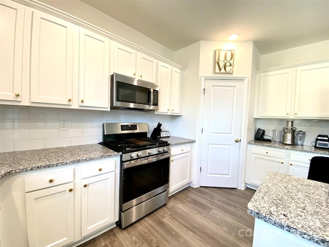 7024 Wheyfield Dr, Charlotte, NC 28215 - kitchen featuring appliances with stainless steel finishes, light wood finished floors, backsplash, white cabinetry, and light stone counters