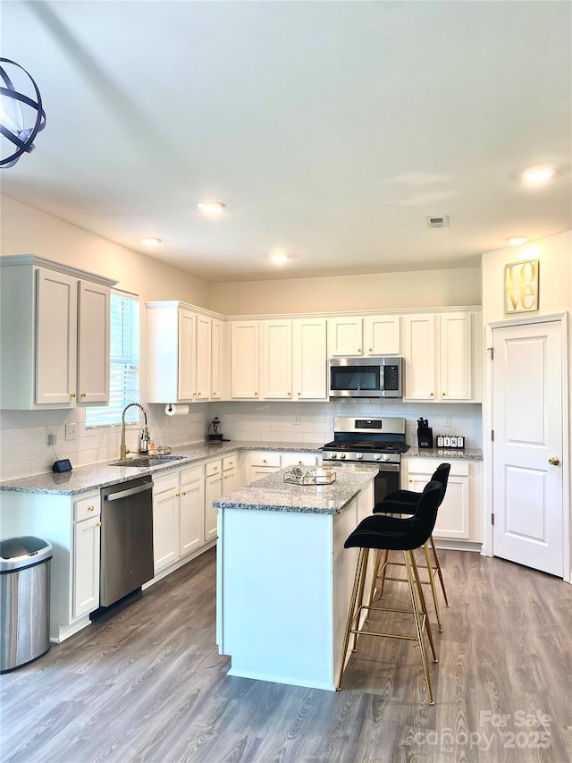 7024 Wheyfield Dr, Charlotte, NC 28215 - kitchen featuring appliances with stainless steel finishes, a sink, a center island, wood finished floors, and backsplash