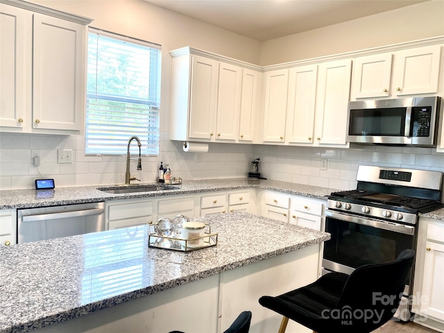 7024 Wheyfield Dr, Charlotte, NC 28215 - kitchen with appliances with stainless steel finishes, a sink, a kitchen bar, white cabinets, and tasteful backsplash