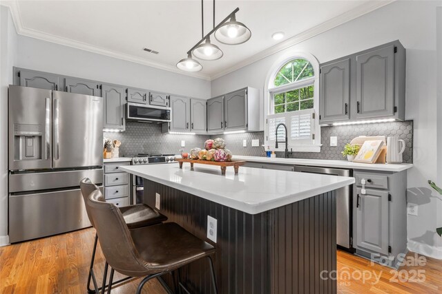 6432 Morningsong Ln, Charlotte, NC 28269 - kitchen with appliances with stainless steel finishes, gray cabinetry, crown molding, light wood-style floors, and decorative backsplash