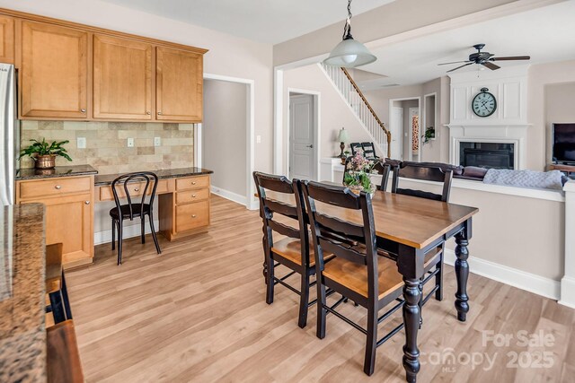 10792 Elsfield Ave NW, Concord, NC 28027 - dining room with baseboards, light wood finished floors, a fireplace, ceiling fan, and stairs