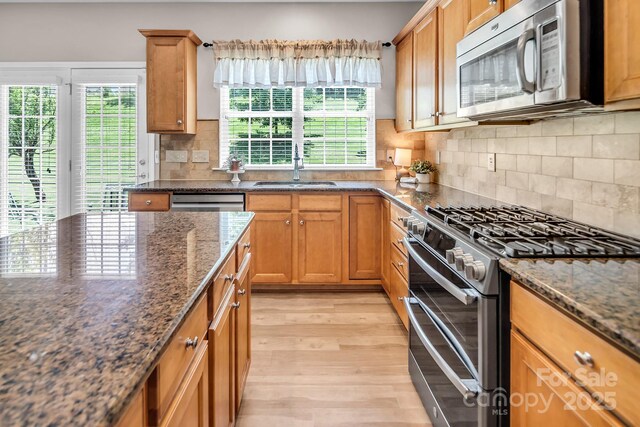 10792 Elsfield Ave NW, Concord, NC 28027 - kitchen with appliances with stainless steel finishes, a sink, light wood-style flooring, dark stone counters, and tasteful backsplash
