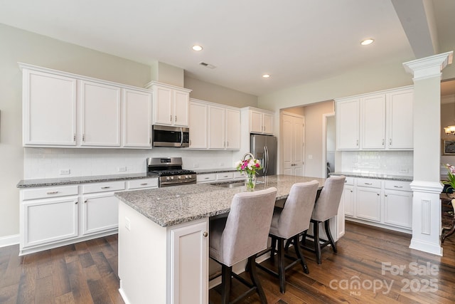 10016 St Kitts Landing Ln, Charlotte, NC 28278 - kitchen featuring stainless steel appliances, ornate columns, white cabinets, dark wood finished floors, and a center island with sink