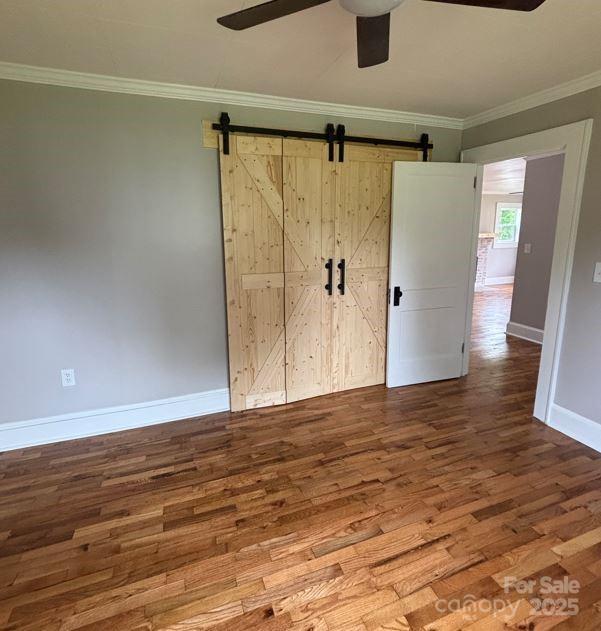410 Gann St, Lowell, NC 28098 - unfurnished bedroom featuring wood finished floors, a barn door, baseboards, crown molding, and a ceiling fan